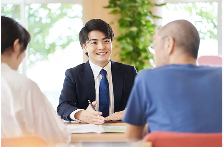 男女のお客様の向かいに座って笑っているスーツ姿の男性